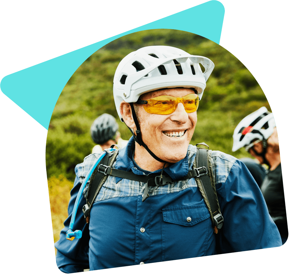 Man smiling wearing white helmet and orange glasses cycling with friends in a nature spot